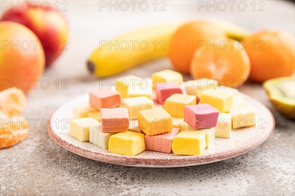 Various fruit jelly chewing candies on plate on brown concrete background. apple, banana, tangerine, side view, close up, selective focus