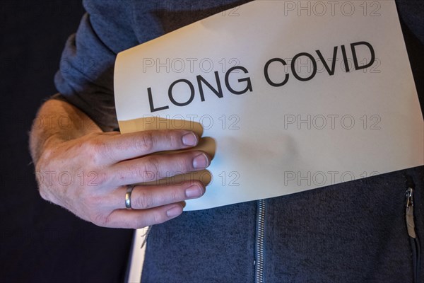 Man holding paper with Long Covid lettering in front of him, studio shot, Germany, Europe