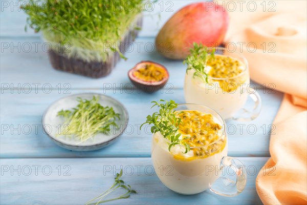 Mango yogurt with passionfruit and cilantro microgreen in glass on blue wooden background with orange linen textile. Side view, close up, selective focus