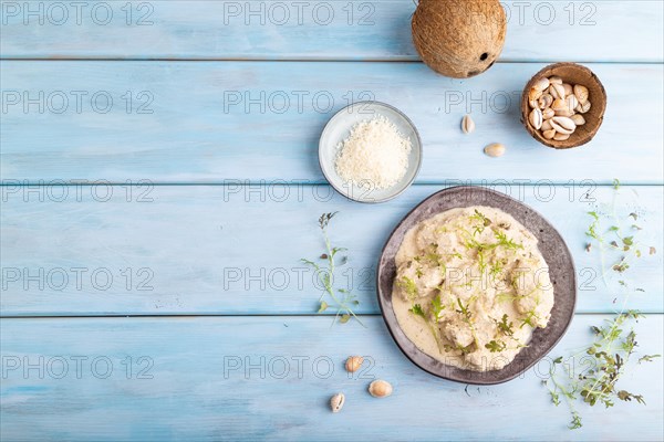 Stewed chicken fillets with coconut milk sauce and mizuna cabbage microgreen on blue wooden background. top view, flat lay, copy space