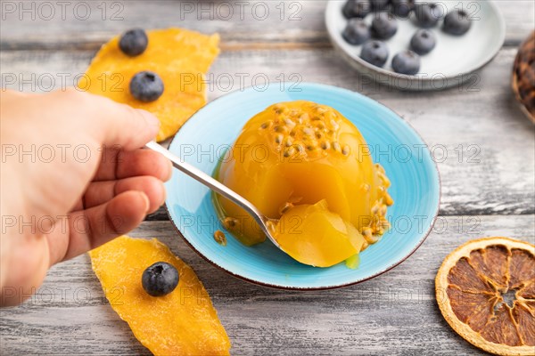 Mango and passion fruit jelly with blueberry with hand on gray wooden background. side view, close up, selective focus
