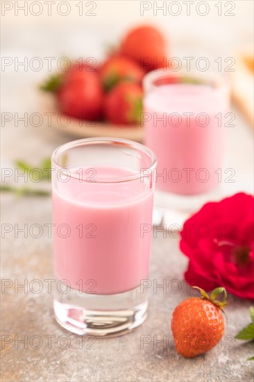 Sweet strawberry liqueur in glass on a gray concrete background and orange textile. side view, close up, selective focus