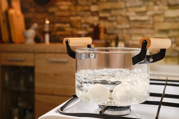 Eggs are boiled in boiling water in a transparent glass saucepan on the stove