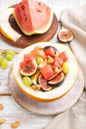 Vegetarian fruit salad of watermelon, grapes, figs, pear, orange, cashew on white wooden background and linen textile. Side view, close up