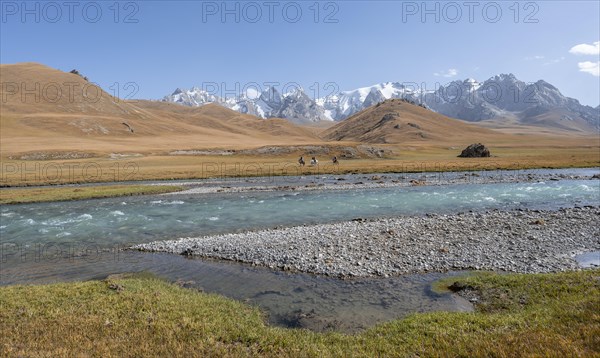 Riders on horses on the river bank, mountain landscape with yellow meadows and river Kol Suu, mountain peak with glacier, hike to the mountain lake Kol Suu, Keltan Mountains, Sary Beles Mountains, Tien Shan, Naryn Province, Kyrgyzstan, Asia