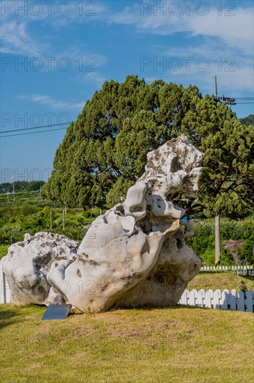 Huge white misshapen boulder on display in rock garden under blue cloudy sky in Gimcheon, South Korea, Asia