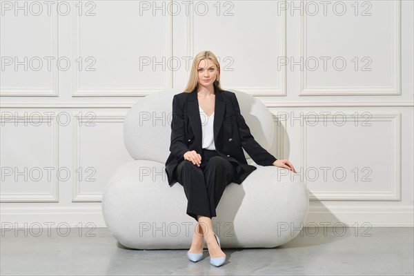 Confident businesswoman in black pantsuit sits on wide bean bag