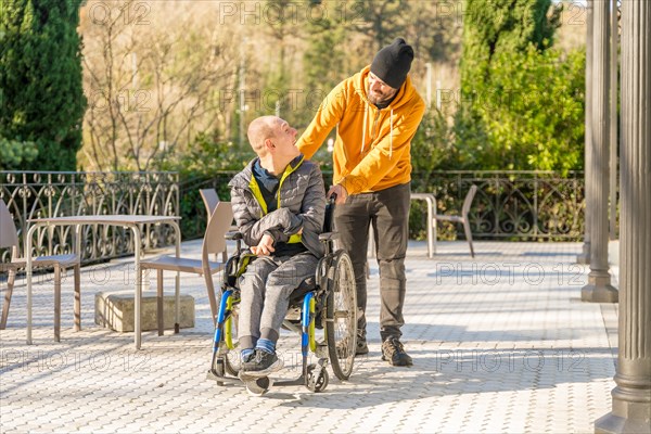 Caregiver pushing the wheelchair of a smiling disabled man in an urban park