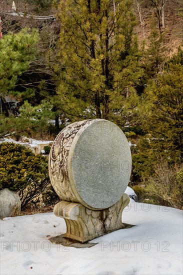 Decorative stone carved Korean drum at Buddhist temple in front of evergreen trees in South Korea