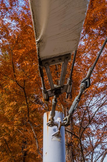 Turnbuckle and support cable attached to flange on white metal pole in public park