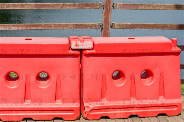 Two red plastic traffic barriers in front of fence on riverside boardwalk