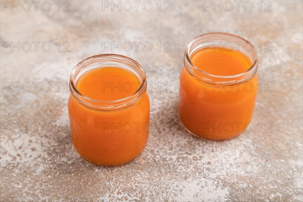 Baby puree with fruits mix, pumpkin, persimmon, mango infant formula in glass jar on brown concrete background. Side view, close up, artificial feeding concept