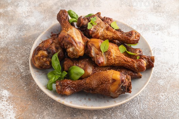 Smoked chicken legs with herbs and spices on a ceramic plate on a brown concrete background. Side view, close up