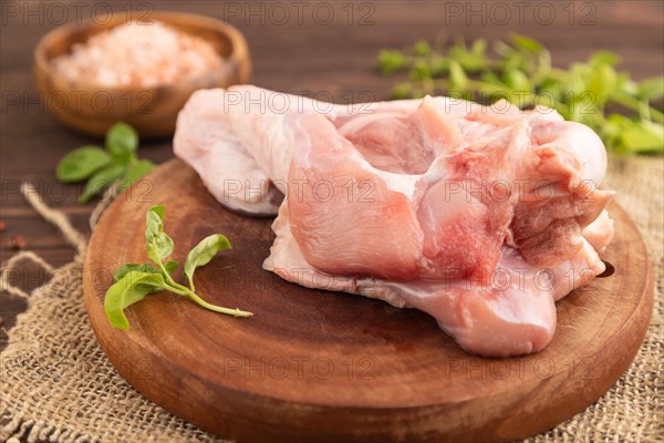 Raw turkey wing with herbs and spices on a wooden cutting board on a brown wooden background and linen textile. Side view, close up, selective focus