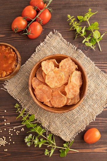 Slices of dehydrated salted meat chips with herbs and spices on brown wooden background and linen textile. Top view, flat lay, close up