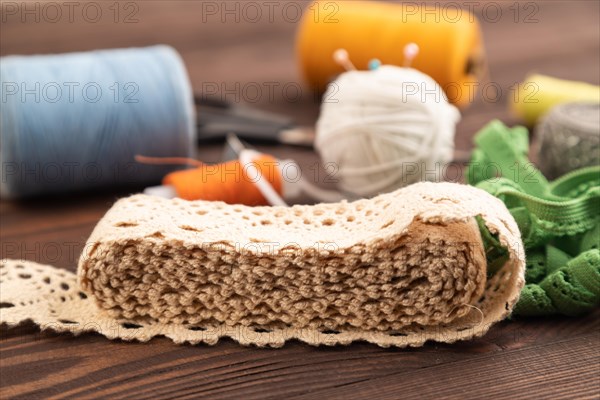 Sewing accessories: scissors, thread, thimbles, braid on brown wooden background. Side view, close up, selective focus