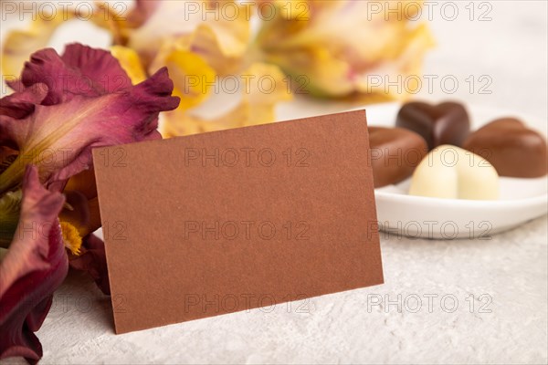 Brown business card with chocolate candies and iris flowers on gray concrete background. side view, copy space, still life. Breakfast, morning, spring concept