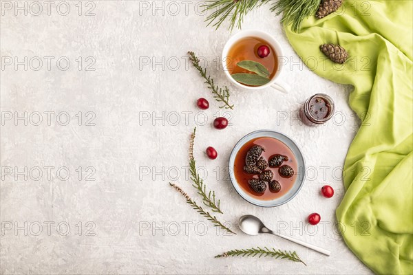 Pine cone jam with herbal tea on gray concrete background and green linen textile. Top view, flat lay, copy space