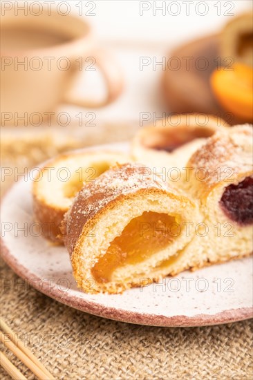 Homemade sweet bun with apricot jam and cup of coffee on white wooden background and linen textile. side view, close up, selective focus