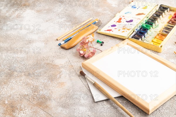 Drawing accessories set: brushes, pencils, watercolor, frame on brown concrete background. Side view, copy space