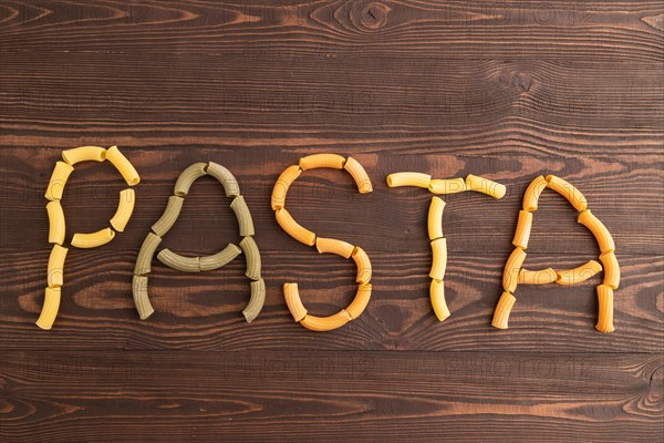 Inscription pasta, Rigatoni colored raw pasta with tomato, eggs, spices, herbs on brown wooden background. Top view, flat lay, copy space