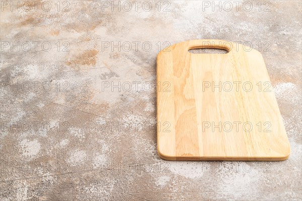 Empty rectangular wooden cutting board on brown concrete background. Side view, copy space