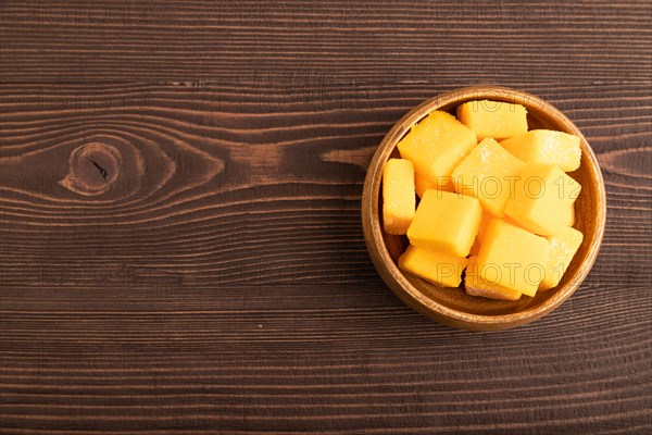 Dried and candied mango cubes in wooden bowls on brown wooden textured background. Top view, flat lay, copy space, vegan, vegetarian food concept