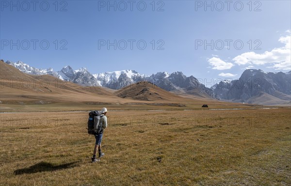 Mountaineer hiking to the mountain lake Kol Suu, mountain landscape with yellow meadows, river Kol Suu and mountain peaks with glacier, Keltan Mountains, Sary Beles Mountains, Tien Shan, Naryn Province, Kyrgyzstan, Asia