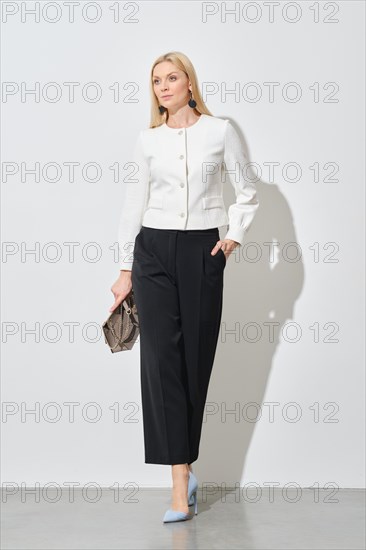 Businesswoman in wide black trousers and short white blazer walking in bright room