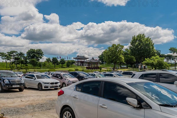 Cars in parking lot with main gate of Hongjueupseong walled town in distance under blue sky in South Korea