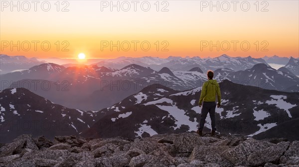 Mountaineer enjoying the view, mountain panorama at the summit of Skala at sunset, sun setting behind the mountains, Loen, Norway, Europe