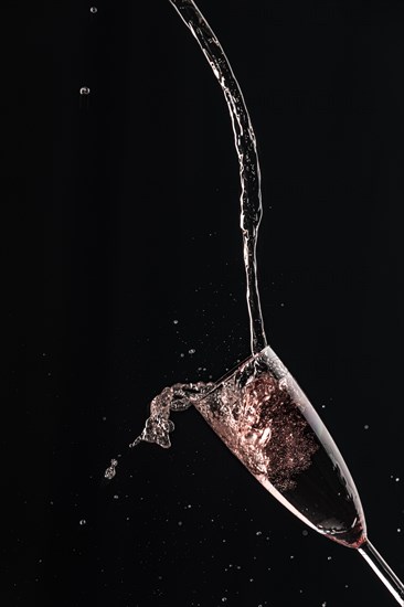 Pink champagne is dynamically poured into a glass, black background