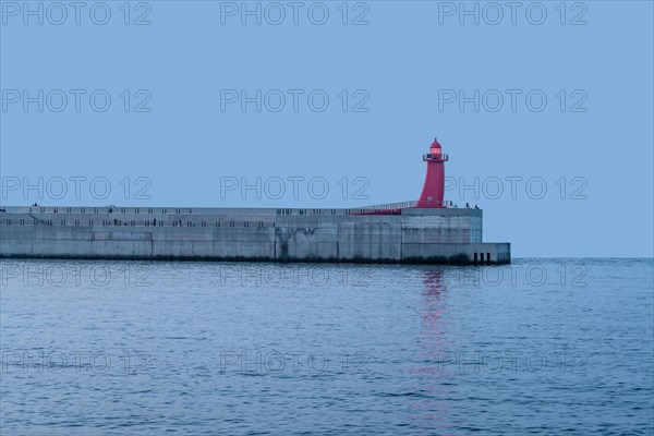 Red lighthouse on end of concrete pier at sunset in Jeju, South Korea, Asia