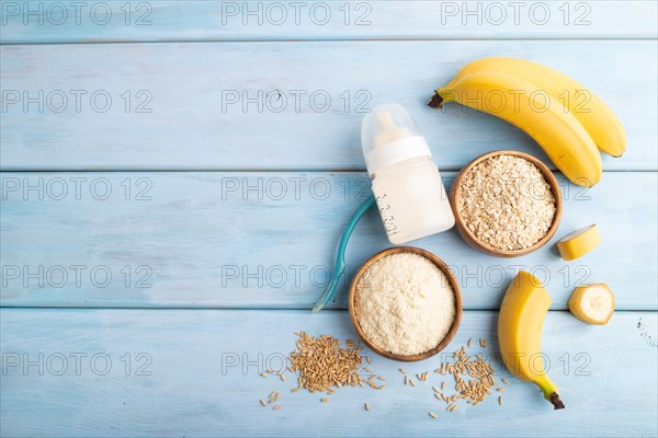 Powdered milk and oatmeal, banana baby food mix, infant formula, pacifier, bottle, spoon on blue wooden background. Top view, flat lay, copy space, artificial feeding concept