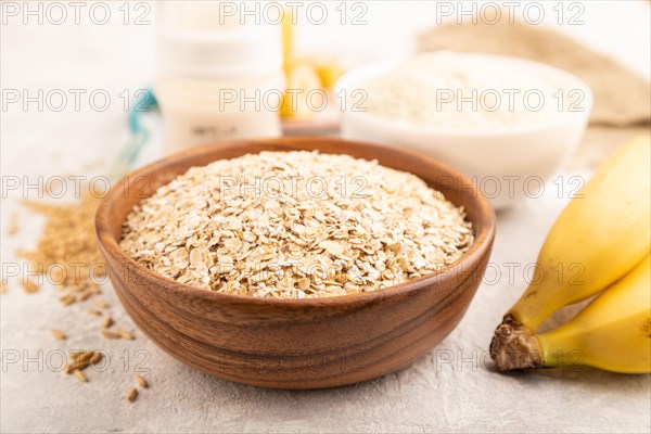 Powdered milk and oatmeal, banana baby food mix, infant formula, pacifier, bottle, spoon on gray concrete background. Side view, close up, selective focus, artificial feeding concept