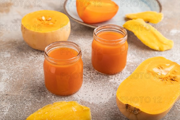 Baby puree with fruits mix, pumpkin, persimmon, mango infant formula in glass jar on brown concrete background. Side view, close up, artificial feeding concept