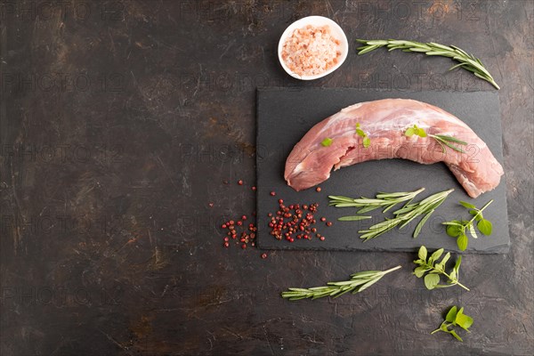 Raw pork meat with herbs and spices on slate cutting board on black concrete background. Top view, flat lay, copy space
