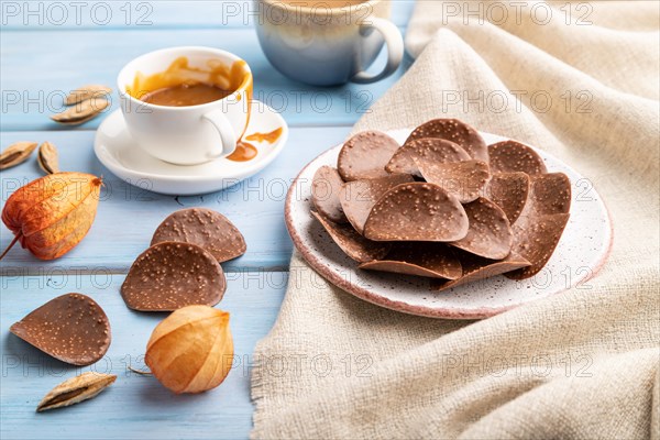 Chocolate chips with cup of coffee and caramel on a blue wooden background and linen textile. side view, close up