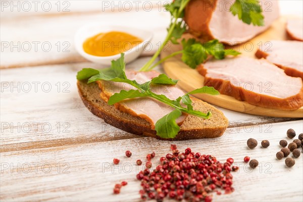 Smoked pork ham on cutting board with pepper and herbs on white wooden background. Side view, close up, selective focus