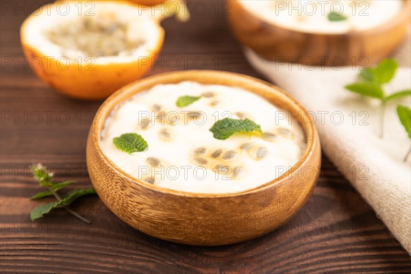 Yoghurt with granadilla and mint in wooden bowl on brown wooden background and linen textile. side view, close up, selective focus