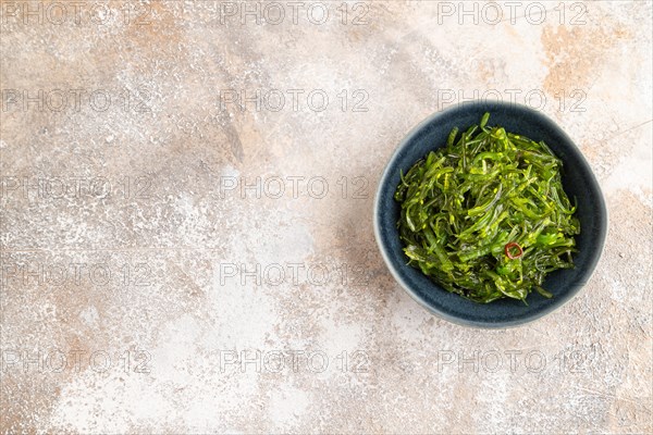 Chuka seaweed salad in blue ceramic bowl on brown concrete background. Top view, flat lay, copy space