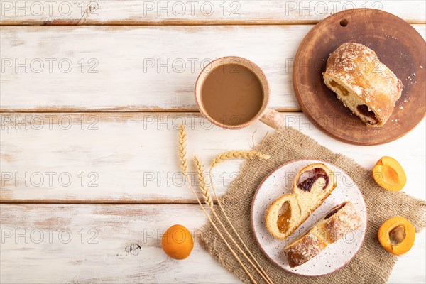 Homemade sweet bun with apricot jam and cup of coffee on white wooden background and linen textile. top view, flat lay, copy space