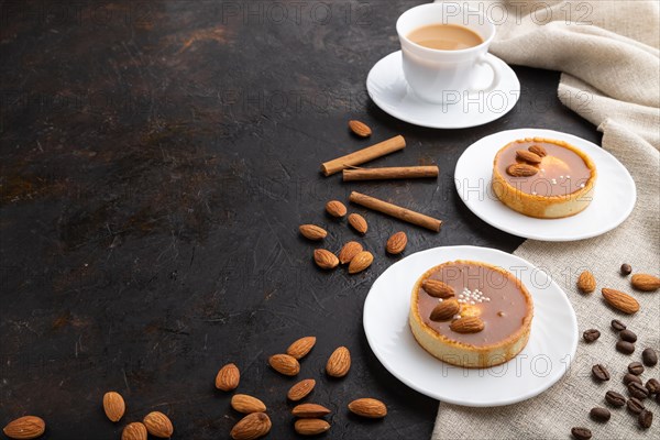 Sweet tartlets with almonds and caramel cream with cup of coffee on a black concrete background and linen textile. Side view, copy space