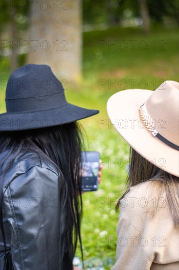 Rear view of two girls looking at the screen of the phone. Back view of two girls in hats looking at the cell phone screen. Concept of two teenage girls looking at the screen of the smart phone