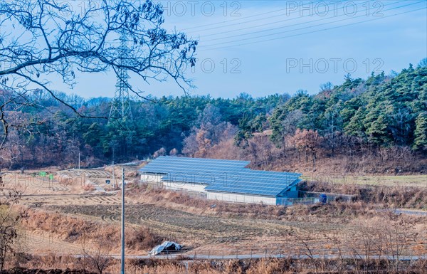 Large array of solar panels setup in countryside in front of hillside covered in lush foliage under blue partly cloudy sky