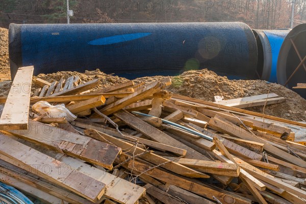 Sections of lumber scattered haphazardly on ground in front of large steel industrial pipes at mountainside construction site