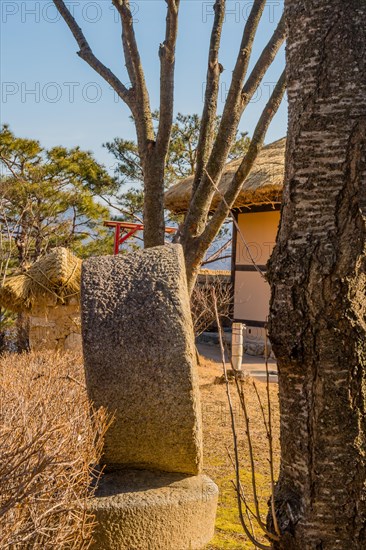 Side view of large millstone on display in public park with thatched roof building in background