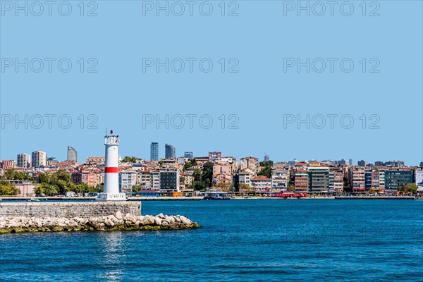 White lighthouse on pier in Bosphorus Strait with city skyline in background in Istanbul, Tuerkiye