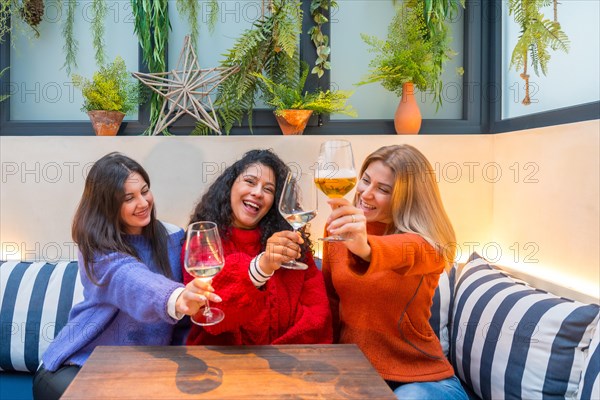 Horizontal photo of three female friends toasting with white wine sitting in a modern colorful cafeteria