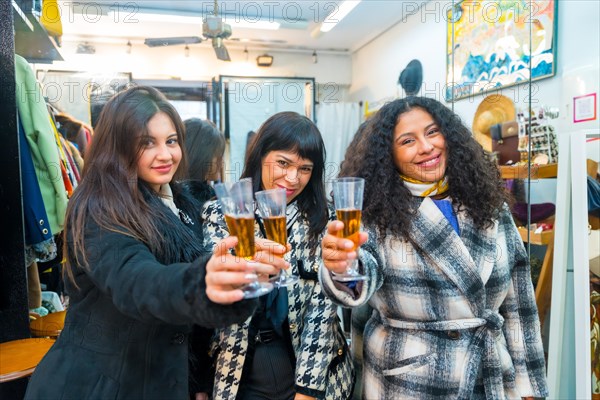 Three woman toasting at camera with champagne in the opening of a fashion store